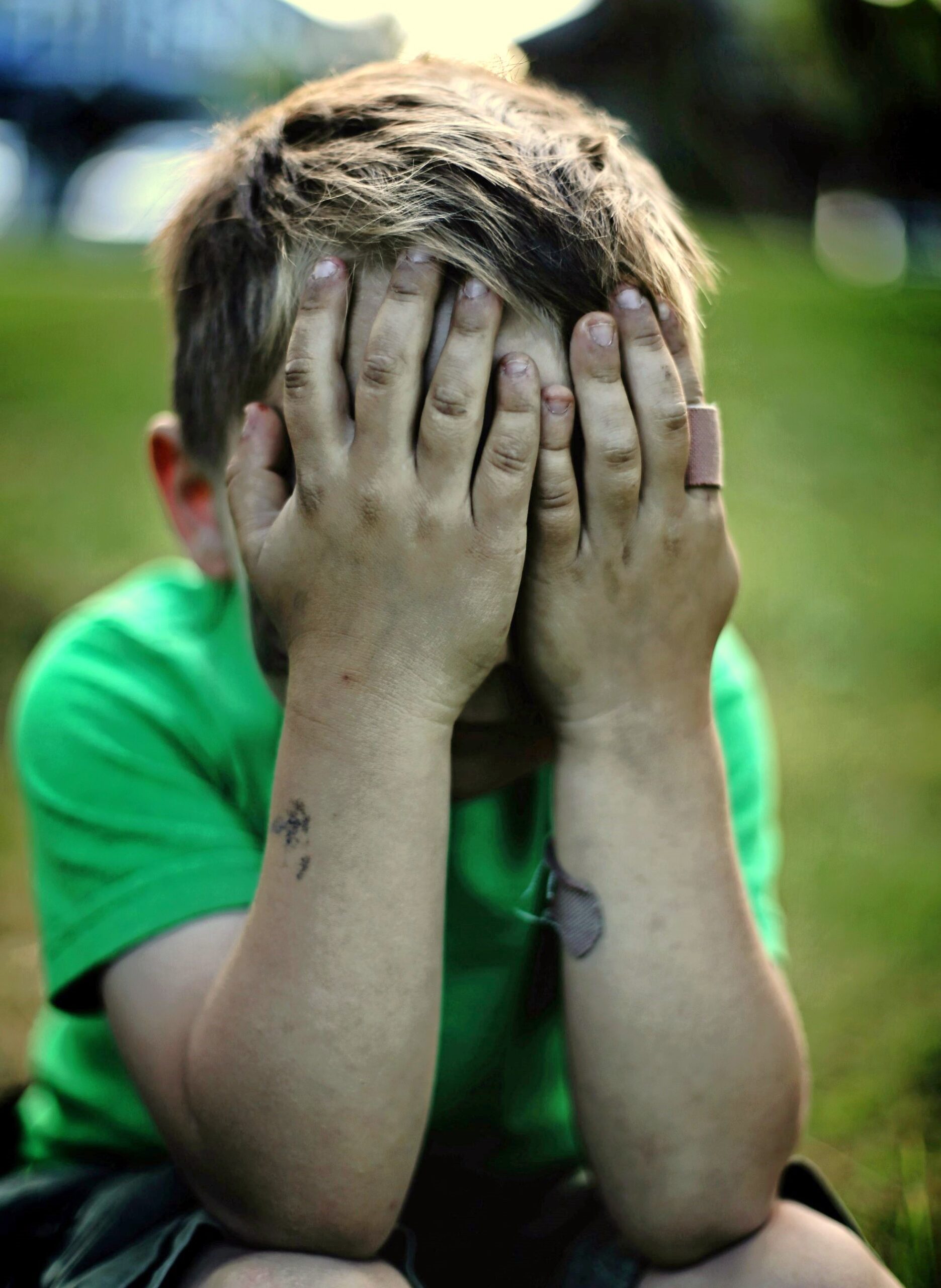 A distressed child covers their face in emotional confusion following misunderstood signs of masturbation and Oppositional Behaviour.