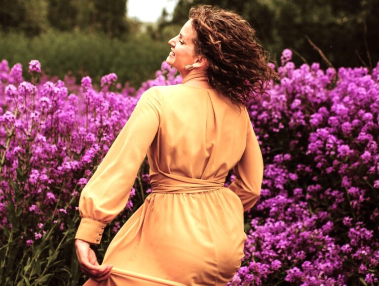 Menopause Libido Solutions shown through a midlife woman spending time alone in nature amongst purple flowers as like an act of self-love.