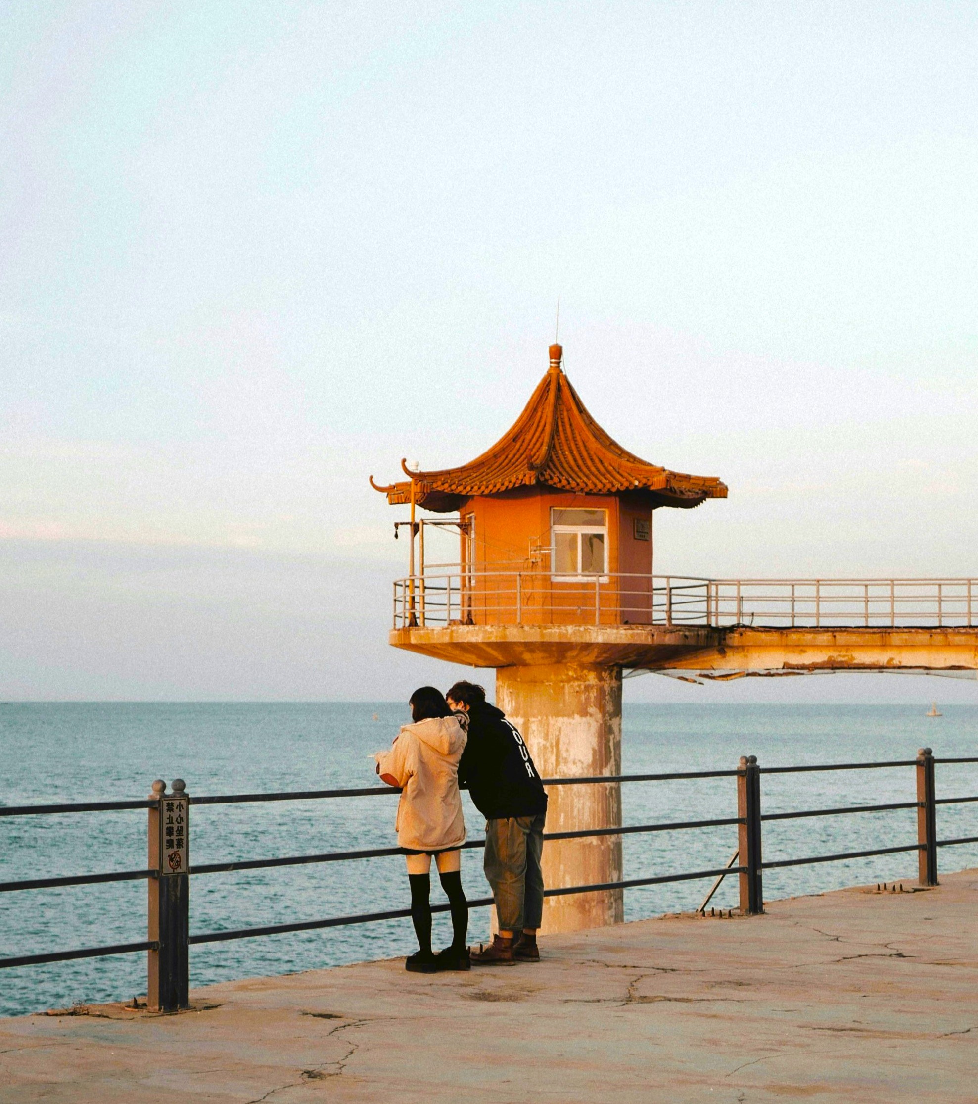 Seaside observation tower with two people standing nearby, engaging in conversation during sunset. The scene evokes feelings of reflection, companionship, and mental wellness amidst a tranquil setting.