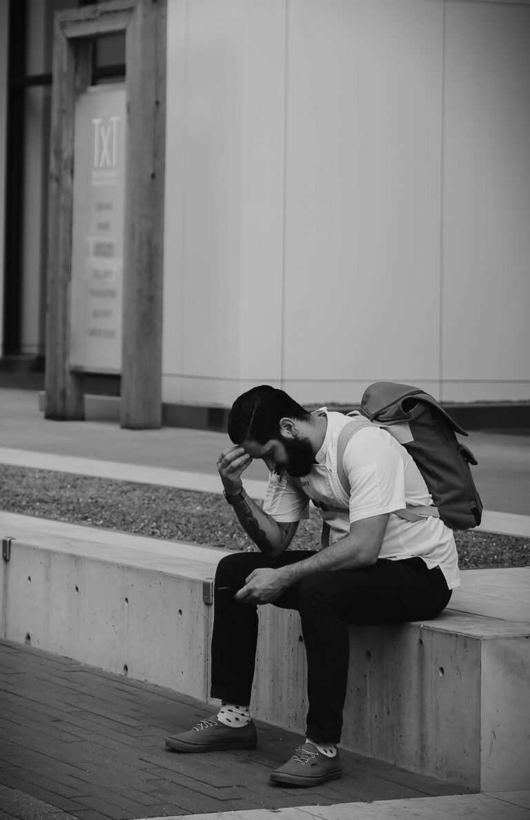Feeling overwhelmed man sitting on bench holding head in distress, reflecting mental health struggles, stress and anxiety in public space, black and white image of emotional distress, mental health support concept.