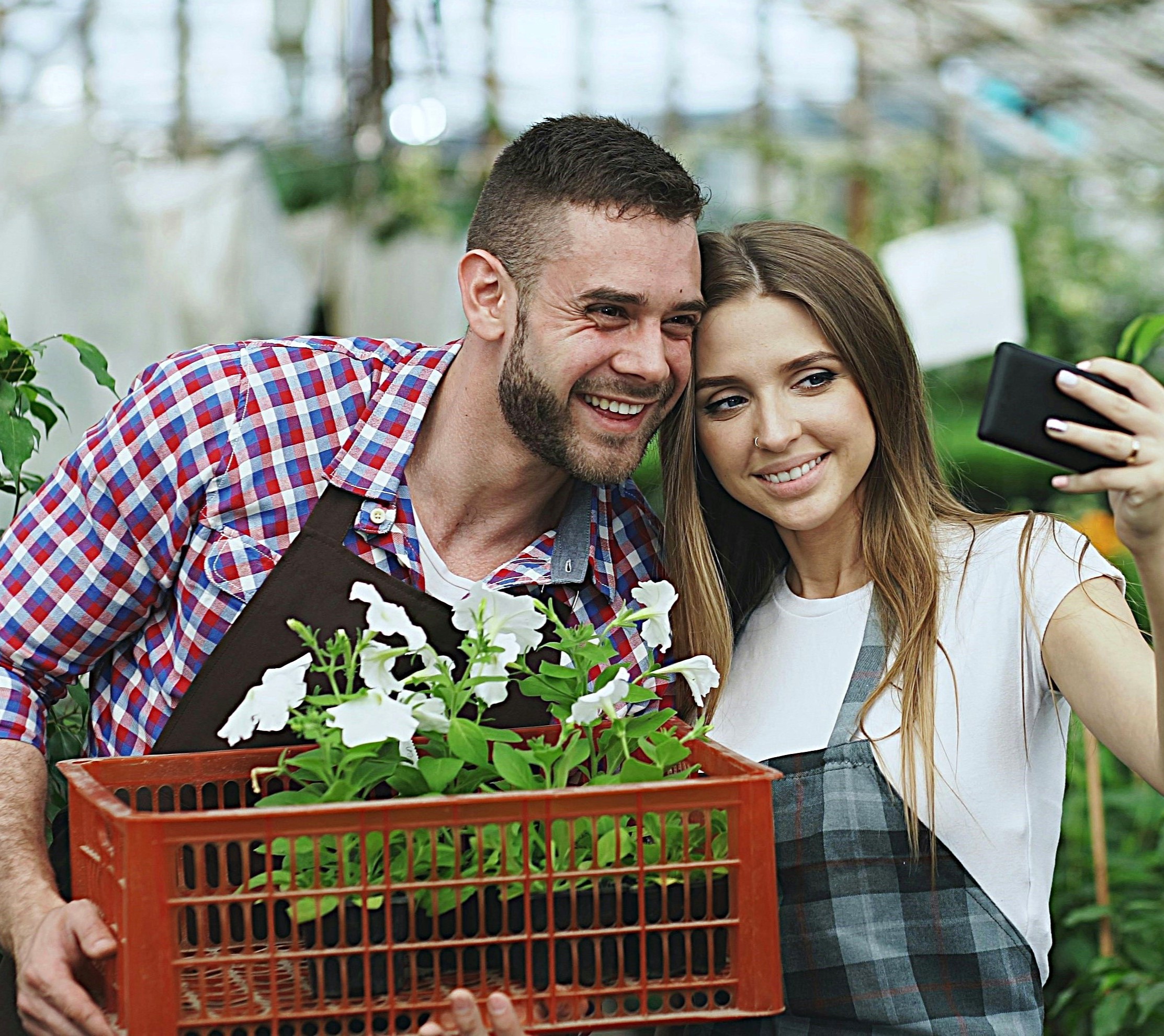 Growing couple smiling while taking a selfie in a greenhouse, representing joy and companionship in mental well-being.