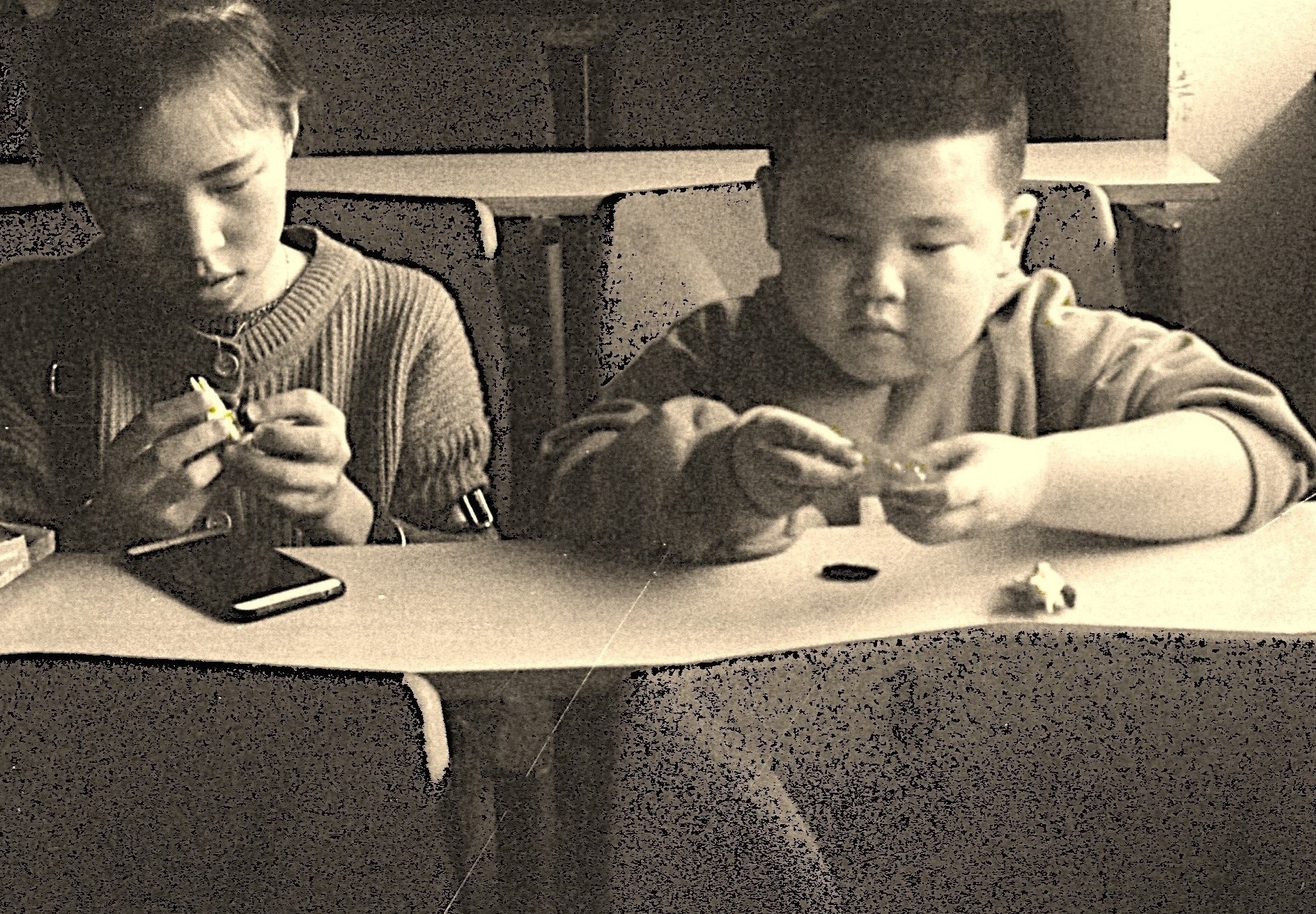 Teens sitting at a table, engaging with small objects, in a classroom setting, indicating focus and concentration.