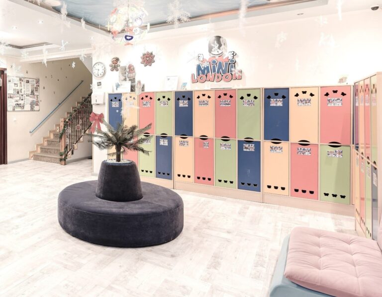 Bright indoor area with colorful lockers, a cozy round seating area, festive decorations, and a sign reading "Mini London," suggesting a children's play or activity centre with a cheerful, welcoming atmosphere.