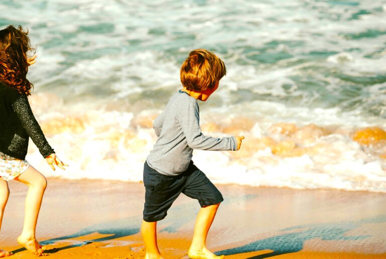 A young boy and girl playing on the beach near the shoreline, exploring and enjoying time outdoors in a natural setting.