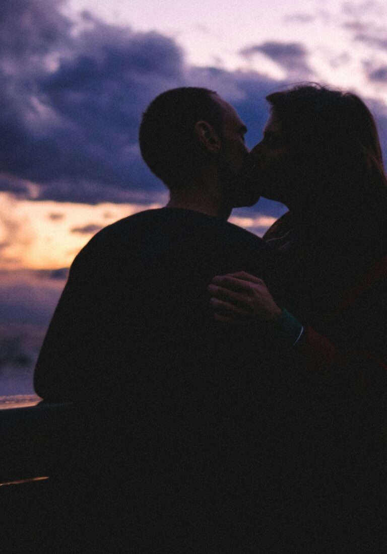 A silhouette of a couple sharing a kiss against a colourful dusk sky, evoking themes of connection, intimacy, and emotional closeness.