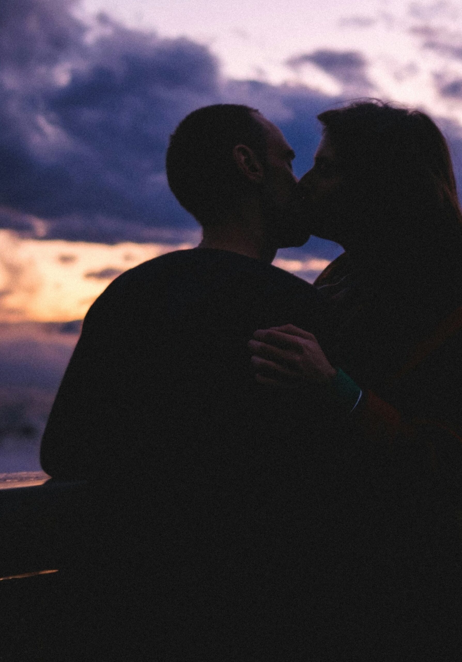 A silhouette of a couple sharing a kiss against a colourful dusk sky, evoking themes of connection, intimacy, and emotional closeness.