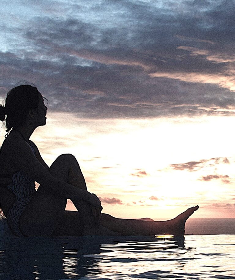 Silhouette of a person by water at sunset, Exploring Emotional Loneliness through self-reflection and personal growth.