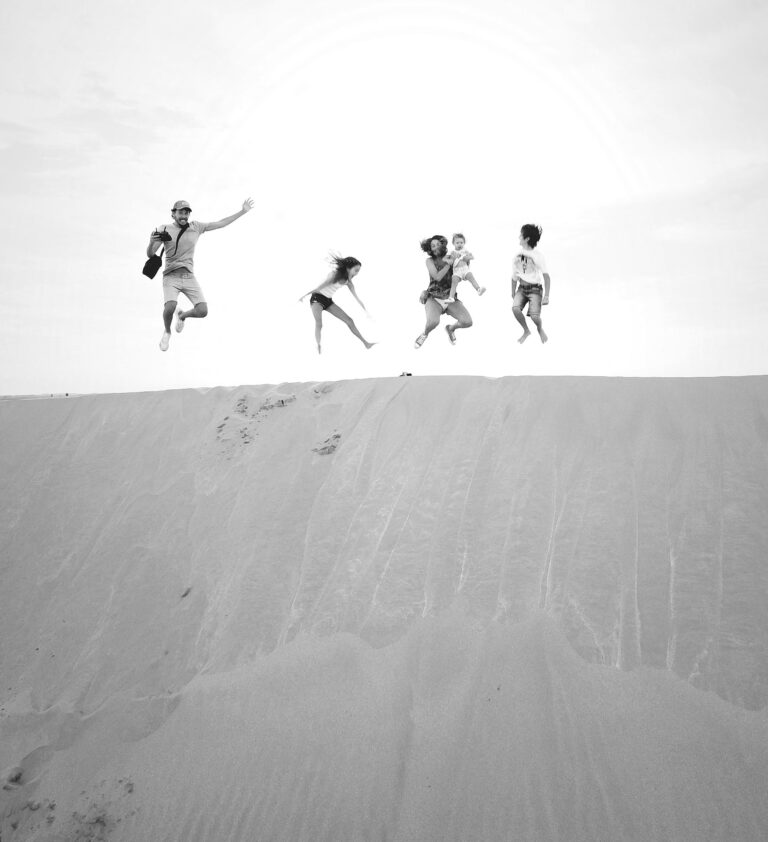 Jumping family on sand dune in desert, black and white.