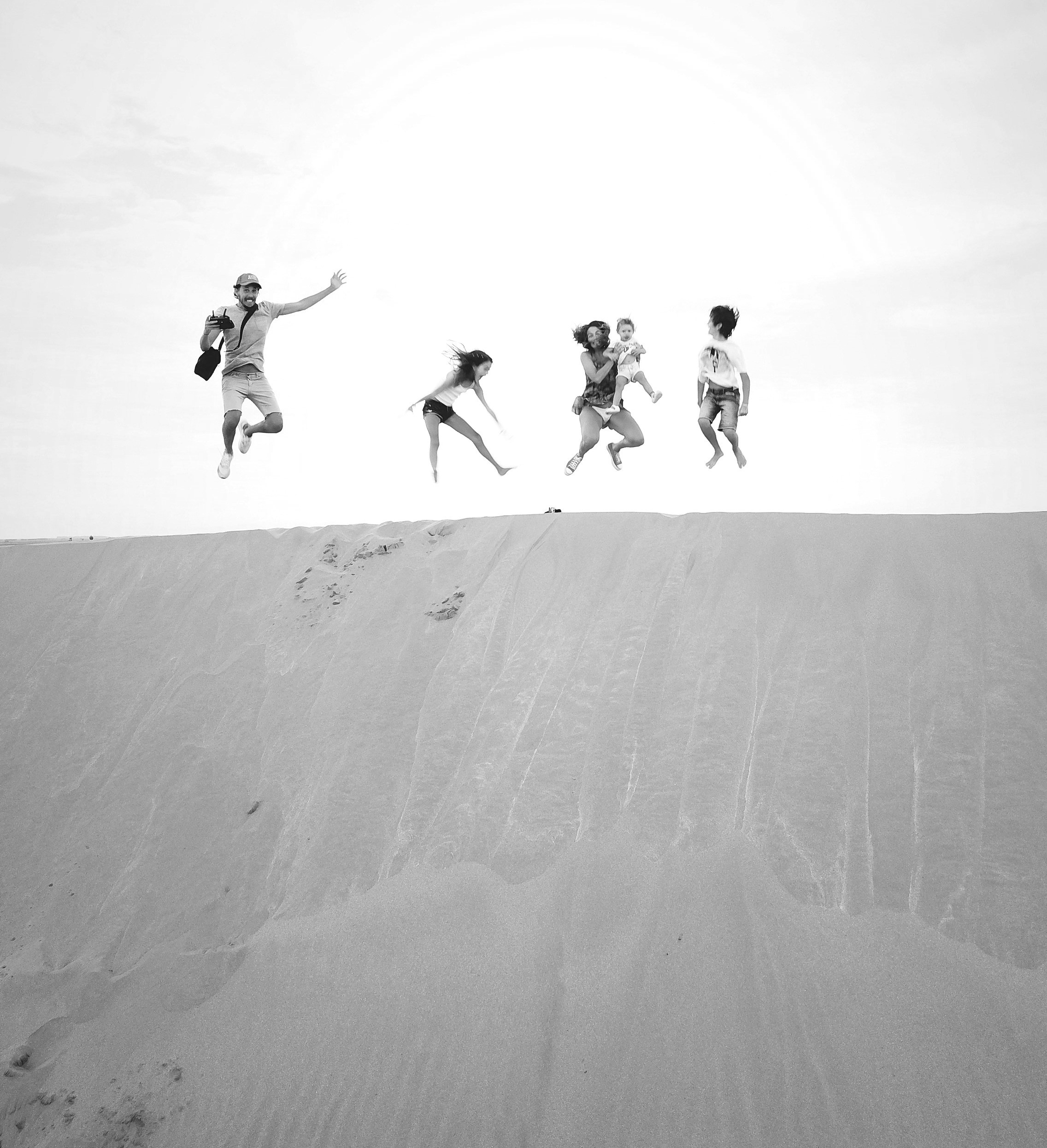 Jumping family on sand dune in desert, black and white.