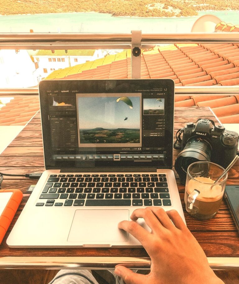 Paragliding footage displayed on a laptop, with a camera, coffee, and a smartphone on a wooden table, capturing outdoor adventure and mental rejuvenation.