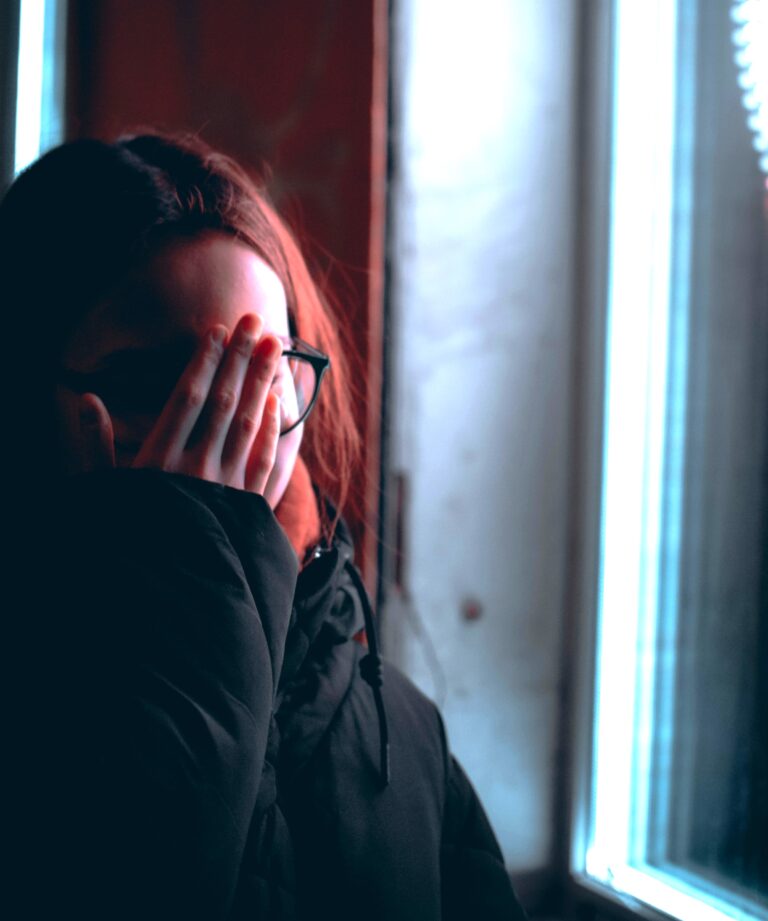 Person covering face in distress by window, symbolising guilt, apology, and Painful Regret after infidelity.