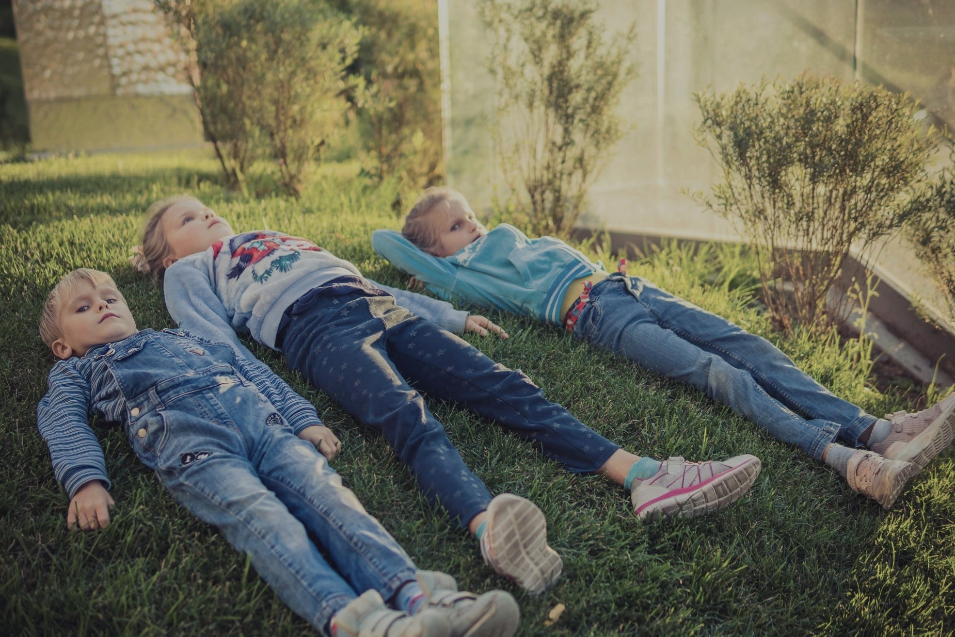 Three kids lying on grass enjoying outdoor time, supporting healthy summer habits in a Fun Educational Summer.