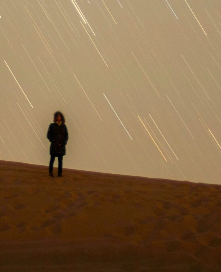 Person stands alone on a dark hill under streaking stars, symbolising reflective solitude and receiving Light Guidance.