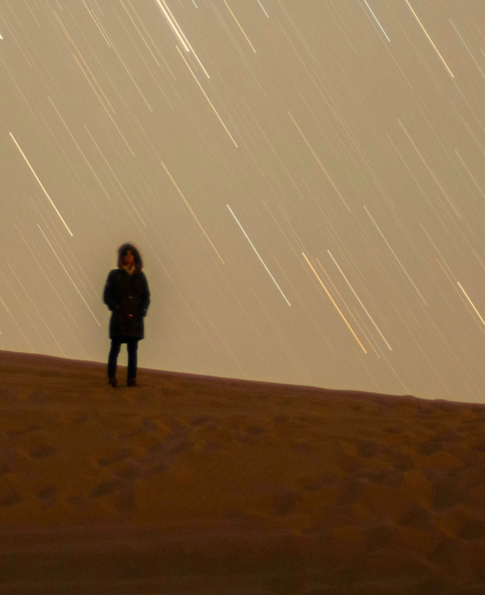 Person stands alone on a dark hill under streaking stars, symbolising reflective solitude and receiving Light Guidance.