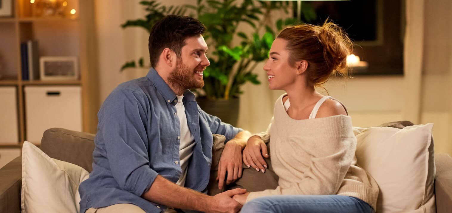Happy couple sharing a moment of connection and intimacy on a sofa, fostering emotional closeness and mental wellbeing in a supportive environment.