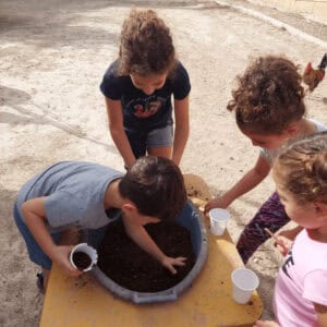 Children engaging in outdoor educational activity, planting seeds or small plants to promote community involvement and environmental awareness.