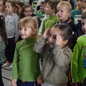 Children gathered together in a classroom or indoor space, displaying various emotional reactions, including curiosity, surprise, and engagement in a group activity or event.