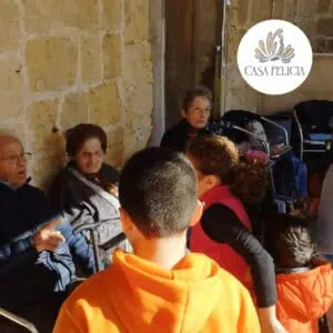 Watching a group of elderly individuals engaged in a discussion in a community or care setting with warm, intimate lighting, promoting mental wellbeing and social connection.