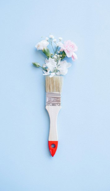 Soft pastel blue background with a paintbrush transforming into a bouquet of delicate, colourful flowers, symbolising growth, healing, and positive change in mental health.