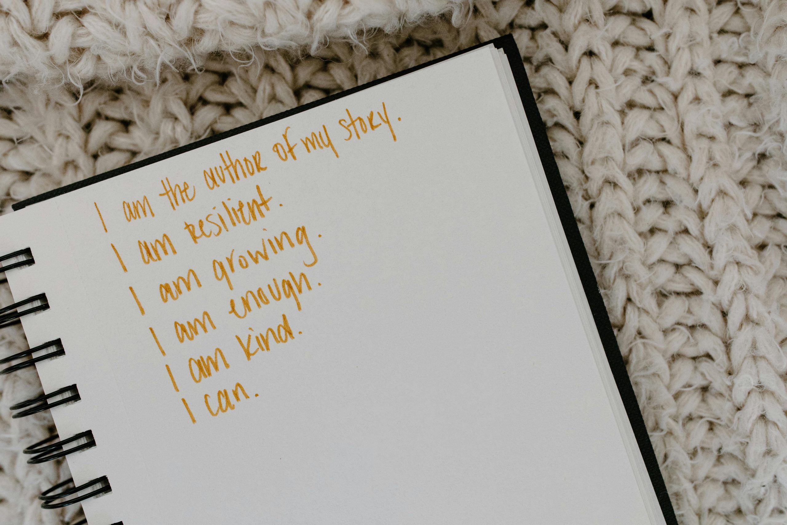 An open notebook is shown with multiple sentences decreasing in length as you go down. Looking closely, you'll spot the word "resilient" in the second sentence from top to bottom. All the sentences are ways of showing that small habits can strengthen resilience.