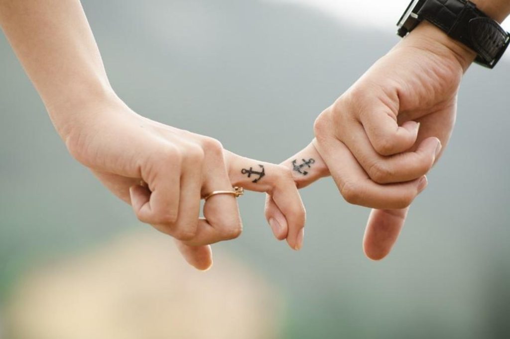 A couple can be seen crossing their pointer fingers (both showing an anchor tattoo) as like an attachment style they use for their relationship.