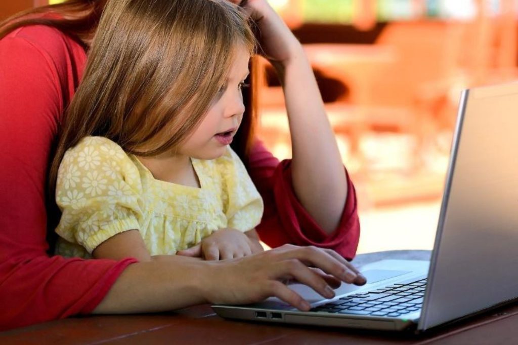 A mother can be seen browsing through her computer with her daughter sitting on her lap. As a mommy blogger, she's making an effort in shaping modern motherhood: support and pressure, as well as realism.