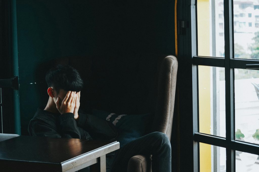 A teenage boy is seen with his hands covering his face in despair, probably since he still needs to learn about healthy ways to express his anger.