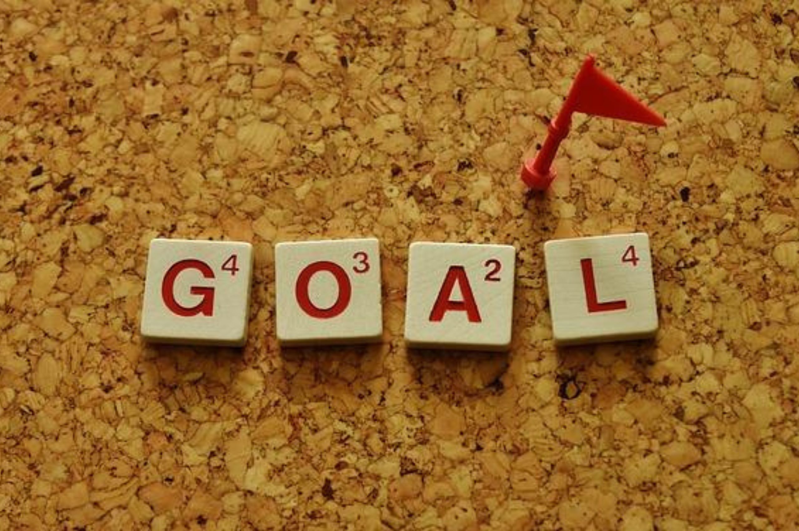 Four individual tiles from a Scrabble board game, with the letters G, O, A, L, spelling out the word GOAL. Message here is to set new goals for new years day that align with you.