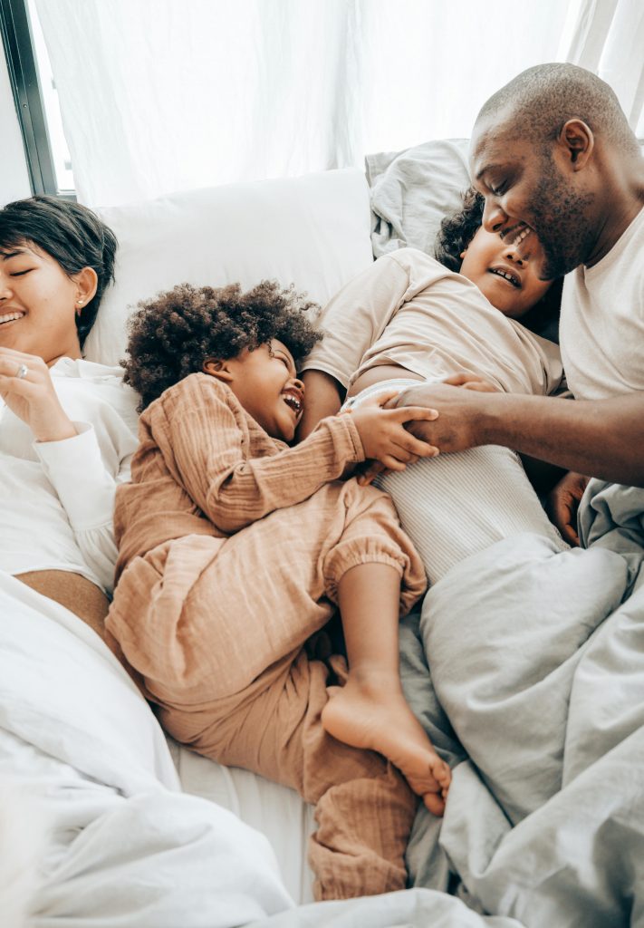 A typical family of four, all smiling because the parents are making an effort in giving their two kids a positive influence via the impact of parental relationships on their choices.