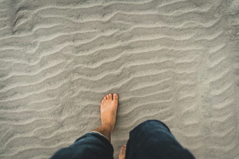 A person feeling the texture of sand under their bare feet, practicing grounding techniques for mindfulness.
