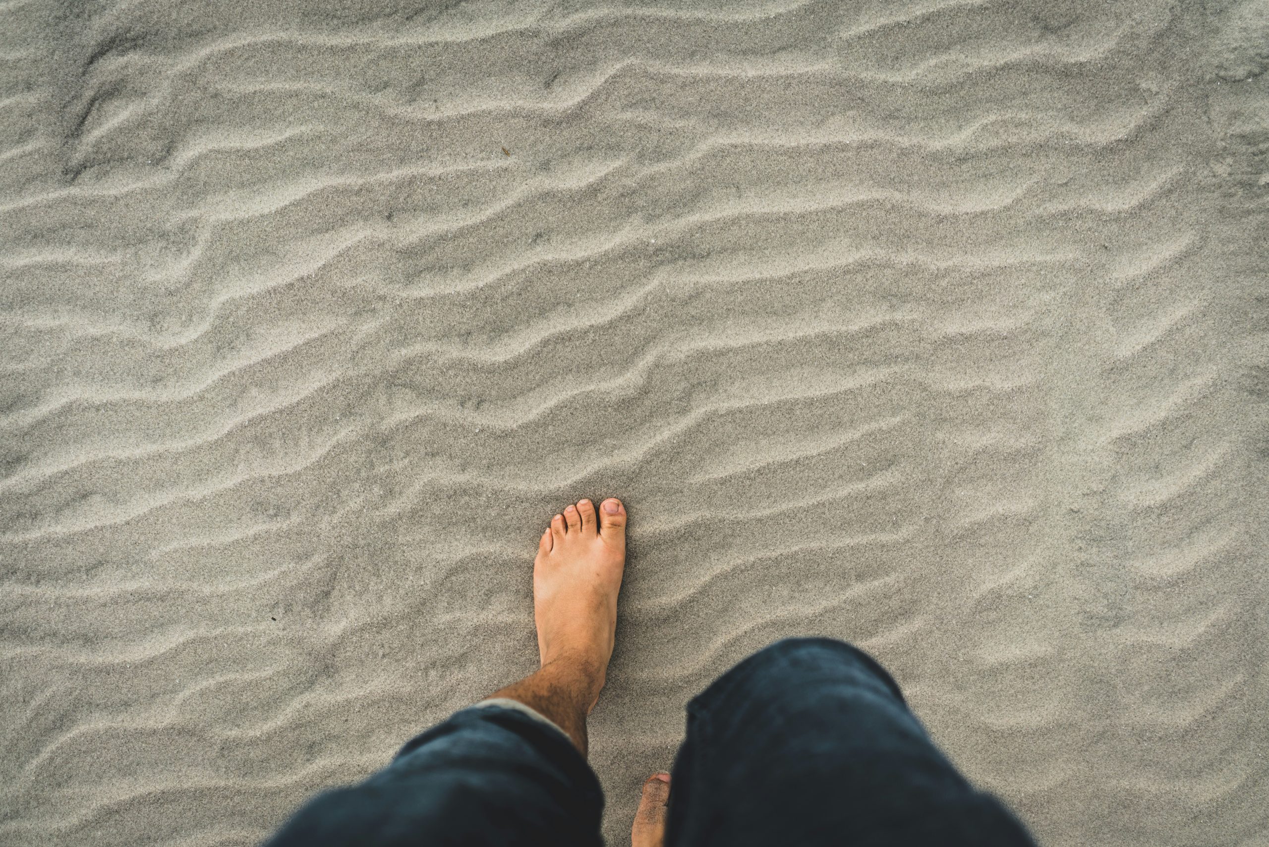 A person feeling the texture of sand under their bare feet, practicing grounding techniques for mindfulness.