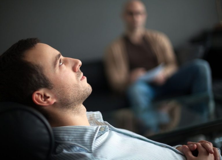 A man lying on a therapist's couch, engaging in EMDR therapy, with the therapist observing in the background.