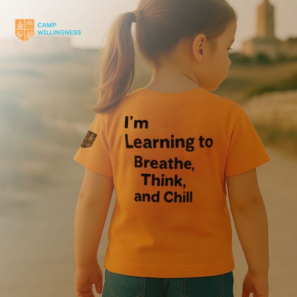 The back of 6 year old girl wearing an orange t-shirt with the text : "I'm learning to brathe, think and chill" and the willingness logo on the right.