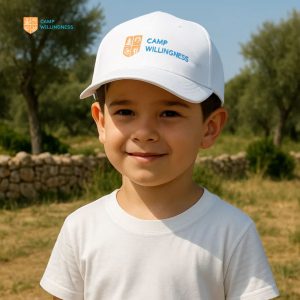 Young boy wearing Camp Willingness Sun Hat outdoors, smiling during summer camp activities.