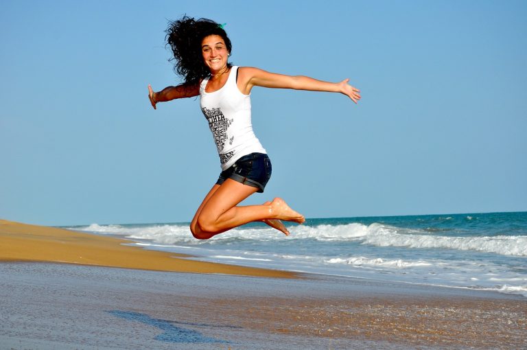 Woman jumping joyfully on the beach, representing the freedom of balancing work and summer fun.
