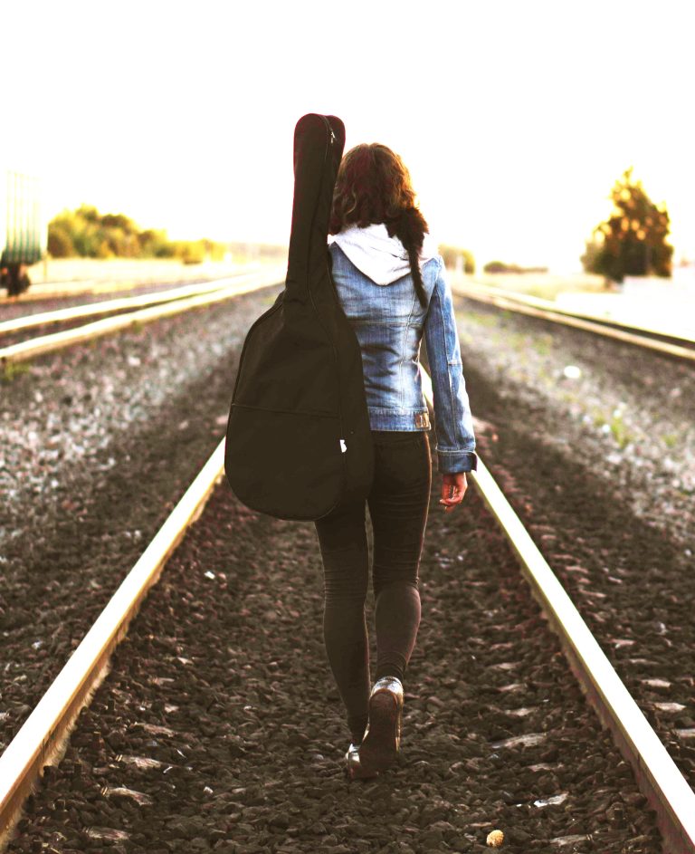 Woman walking on tracks with guitar, finding purpose when feeling lost.