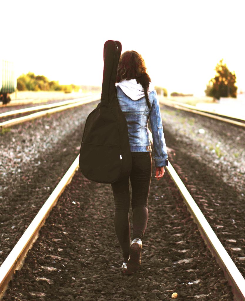 Woman walking on tracks with guitar, finding purpose when feeling lost.