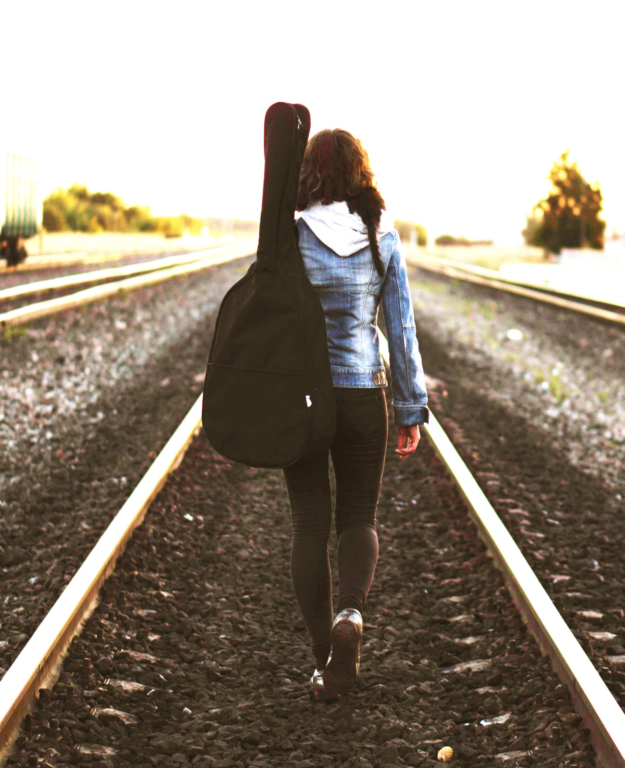 Woman walking on tracks with guitar, finding purpose when feeling lost.