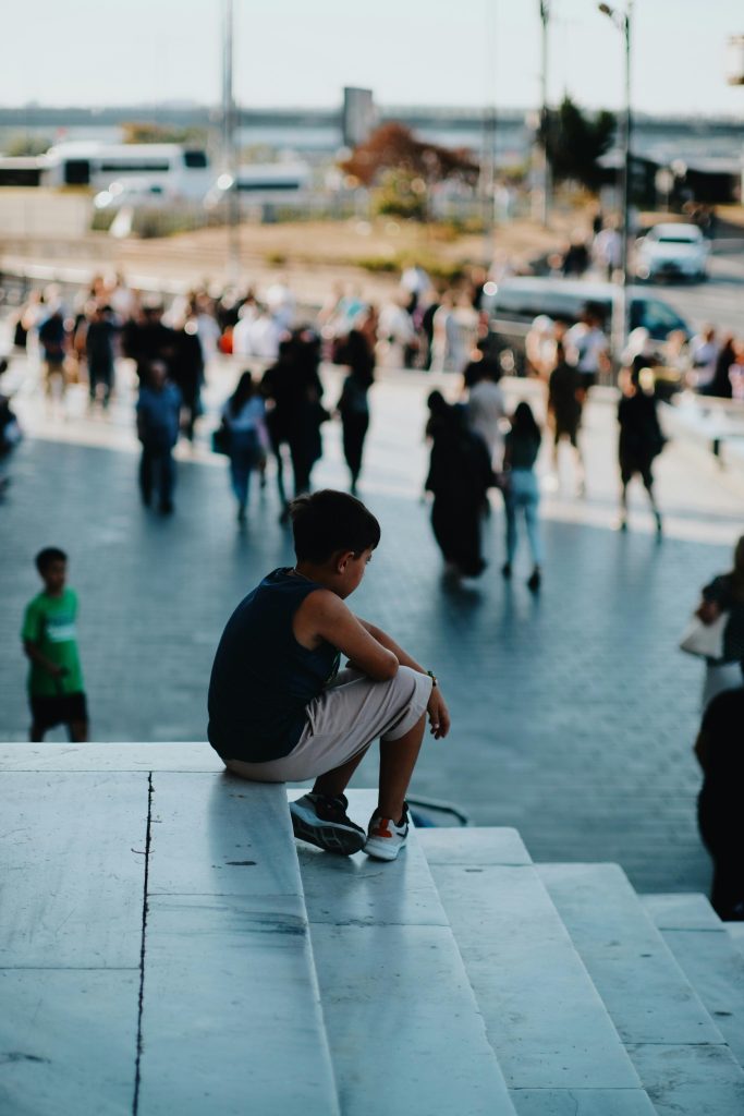 Boy sitting alone on steps in a crowd, symbolising building meaningful relationships.