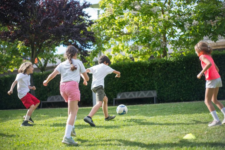 A group of young children are shown playing football in the backyard during the summer time. Kids can actually benefit a lot from summer activities.