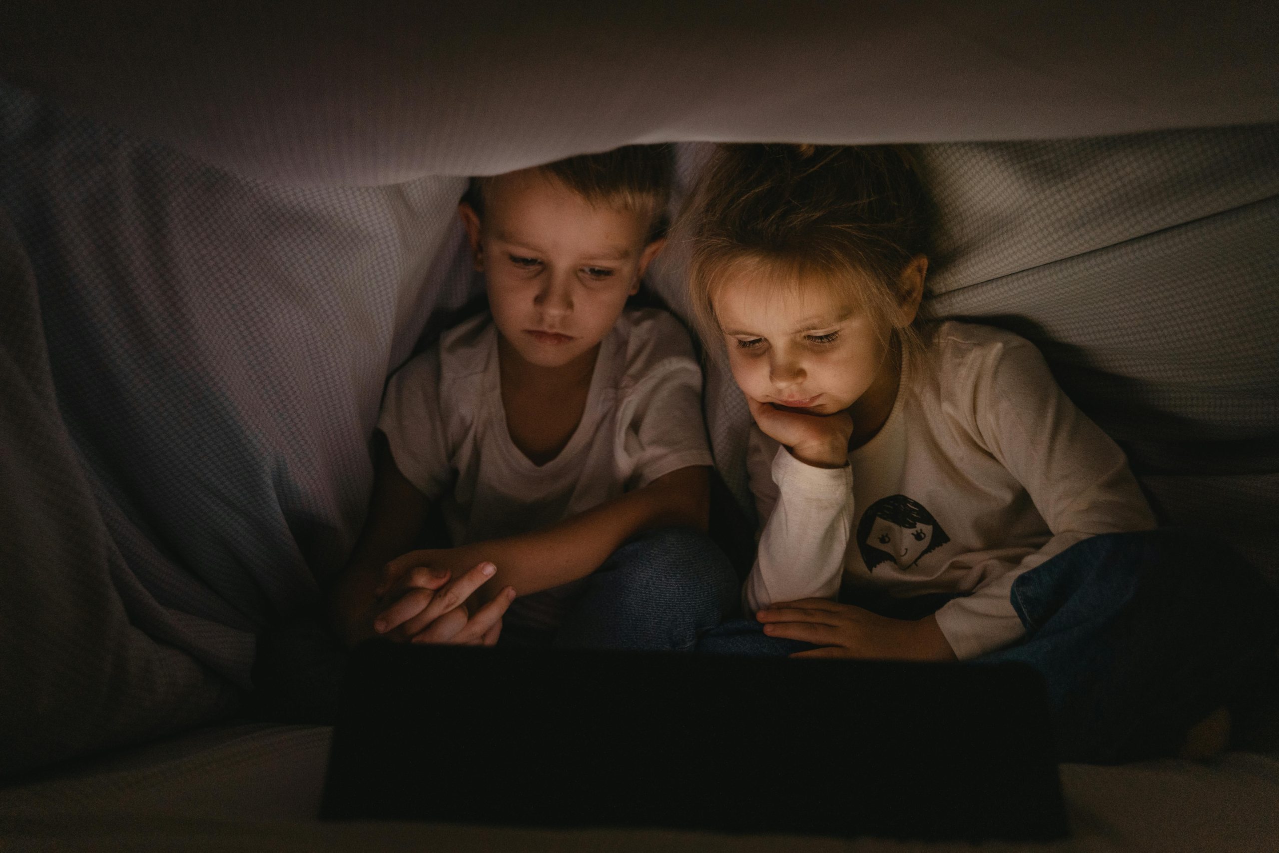 Two kids using a tablet in the dark, showing why kids can't switch off screens.