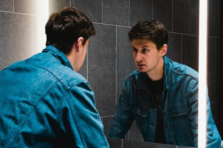 Man looking at himself in the mirror, reflecting inner self-criticism and emotional struggle.