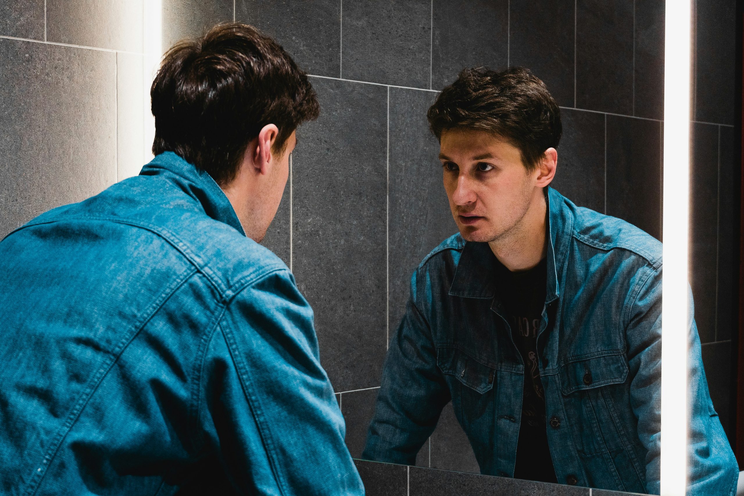 Man looking at himself in the mirror, reflecting inner self-criticism and emotional struggle.
