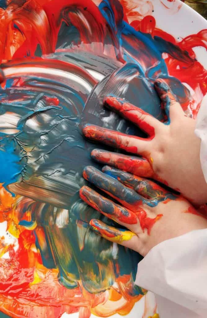 Swirling colourful paint on a canvas with a hand covered in paint, symbolising emotional expression and mental health therapy.