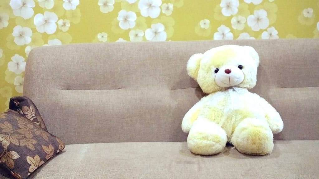 Soft yellow teddy bear placed on a beige sofa with a floral wallpaper background, creating a comforting and calming atmosphere.