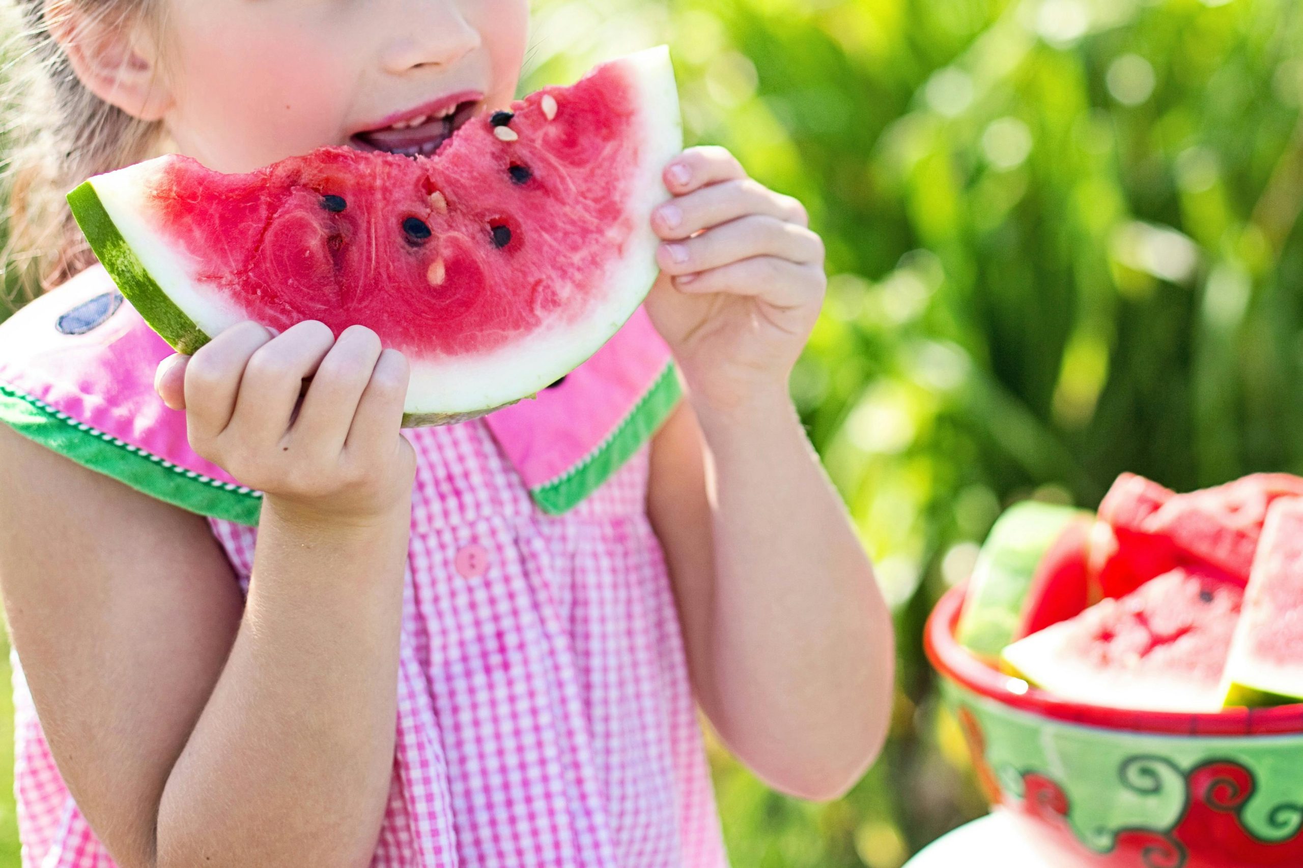 Child enjoying fresh watermelon outdoors for summer hydration tips.