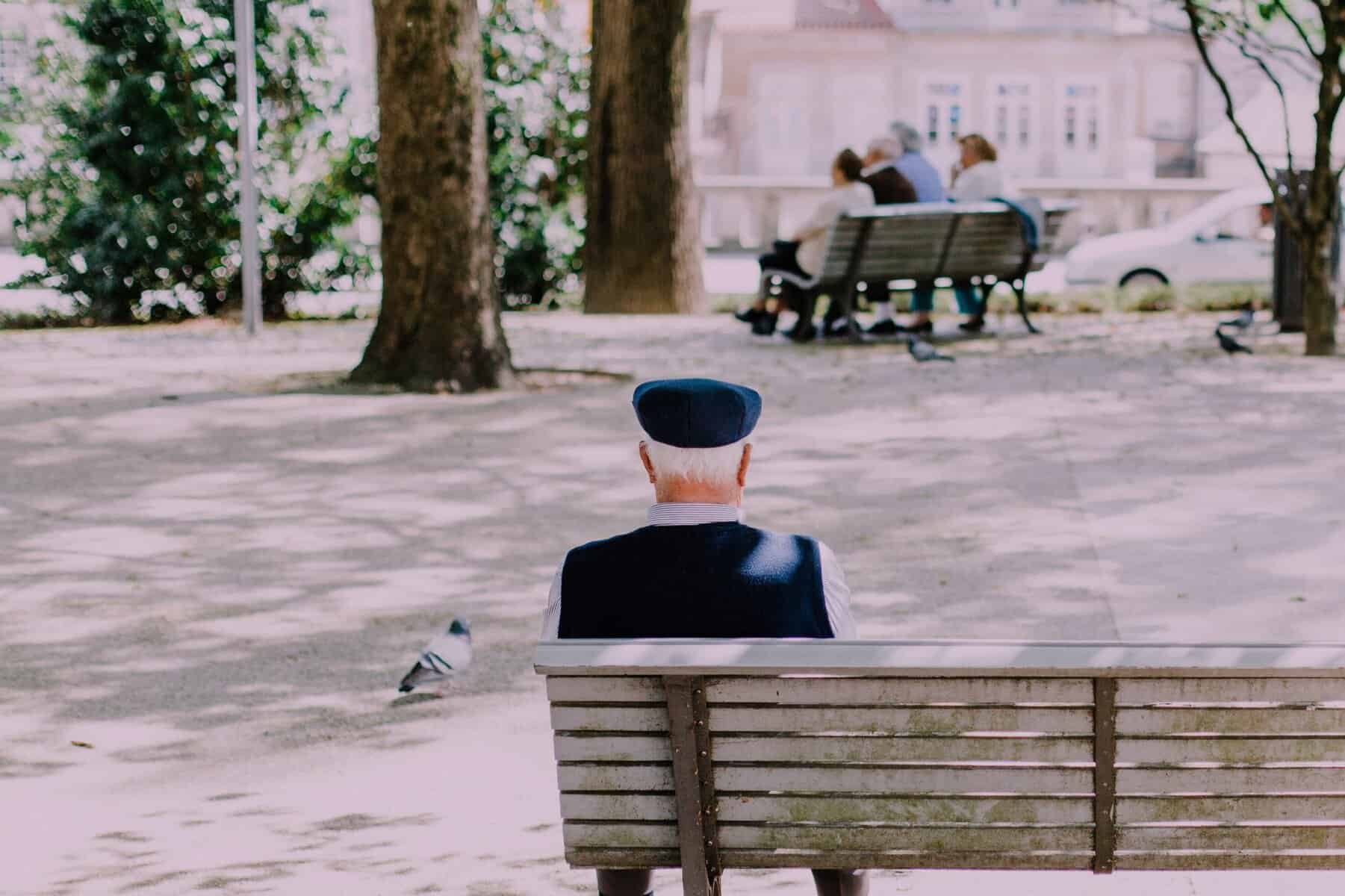 Contemplative elderly man sitting alone on a park bench, reflecting on life amidst trees and nature, symbolising themes of solitude, mindfulness, and mental well-being.