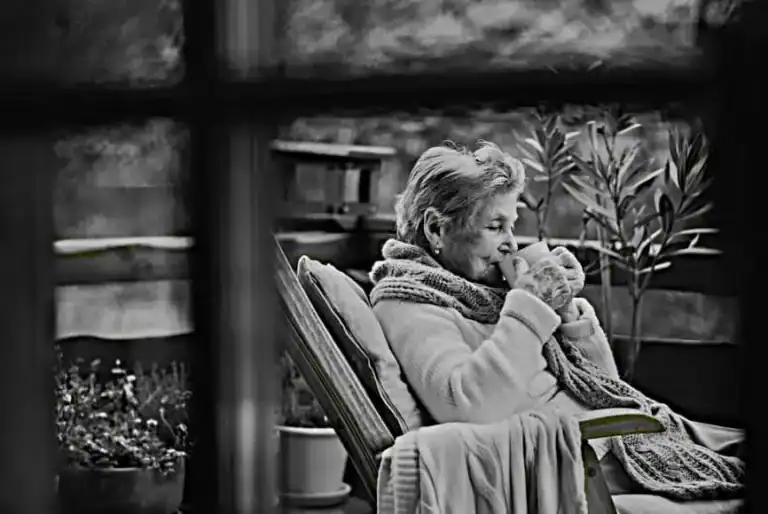Relaxing elderly woman enjoying a warm drink outdoors, symbolising comfort and mindfulness, suitable for mental health and self-care content.