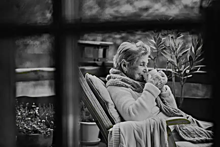 Relaxing elderly woman enjoying a warm drink outdoors, symbolising comfort and mindfulness, suitable for mental health and self-care content.