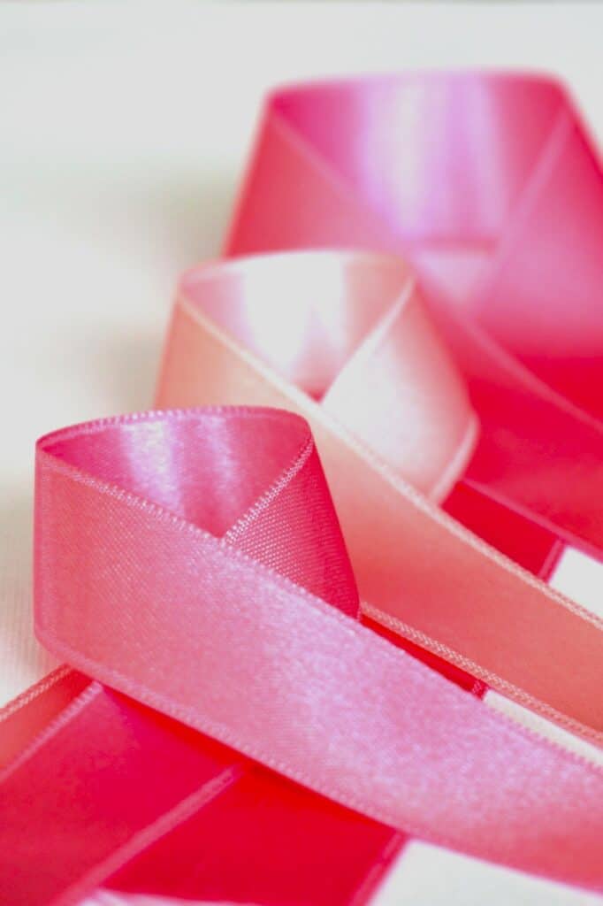 Three satin pink ribbons curled on white background to represent Vigilant Care For Women during breast cancer.